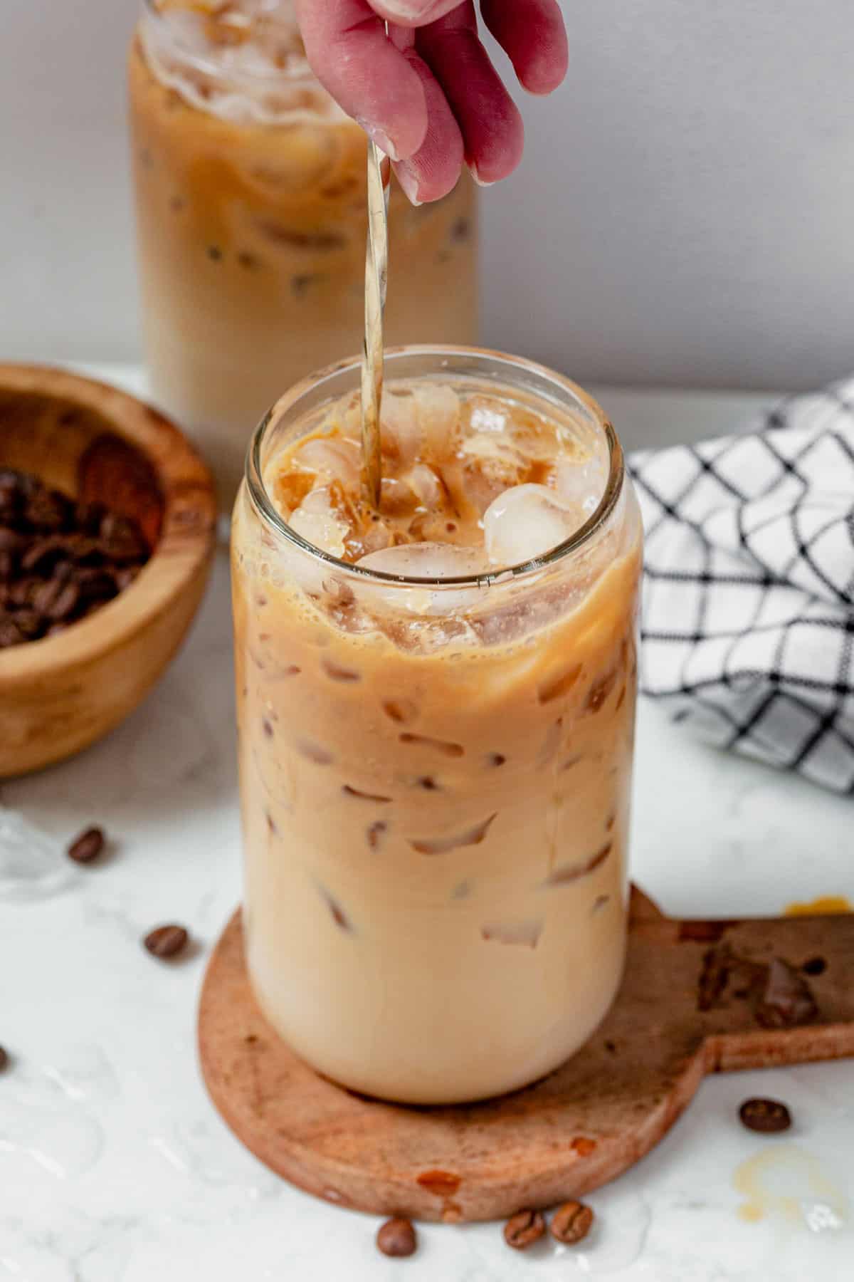 stirring an iced protein coffee in a tall glass with a spoon.
