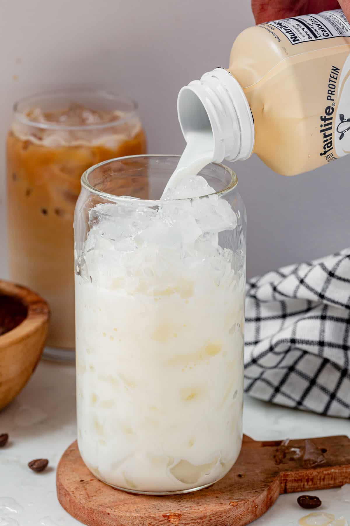 pouring a vanilla protein shake into a cup with ice.