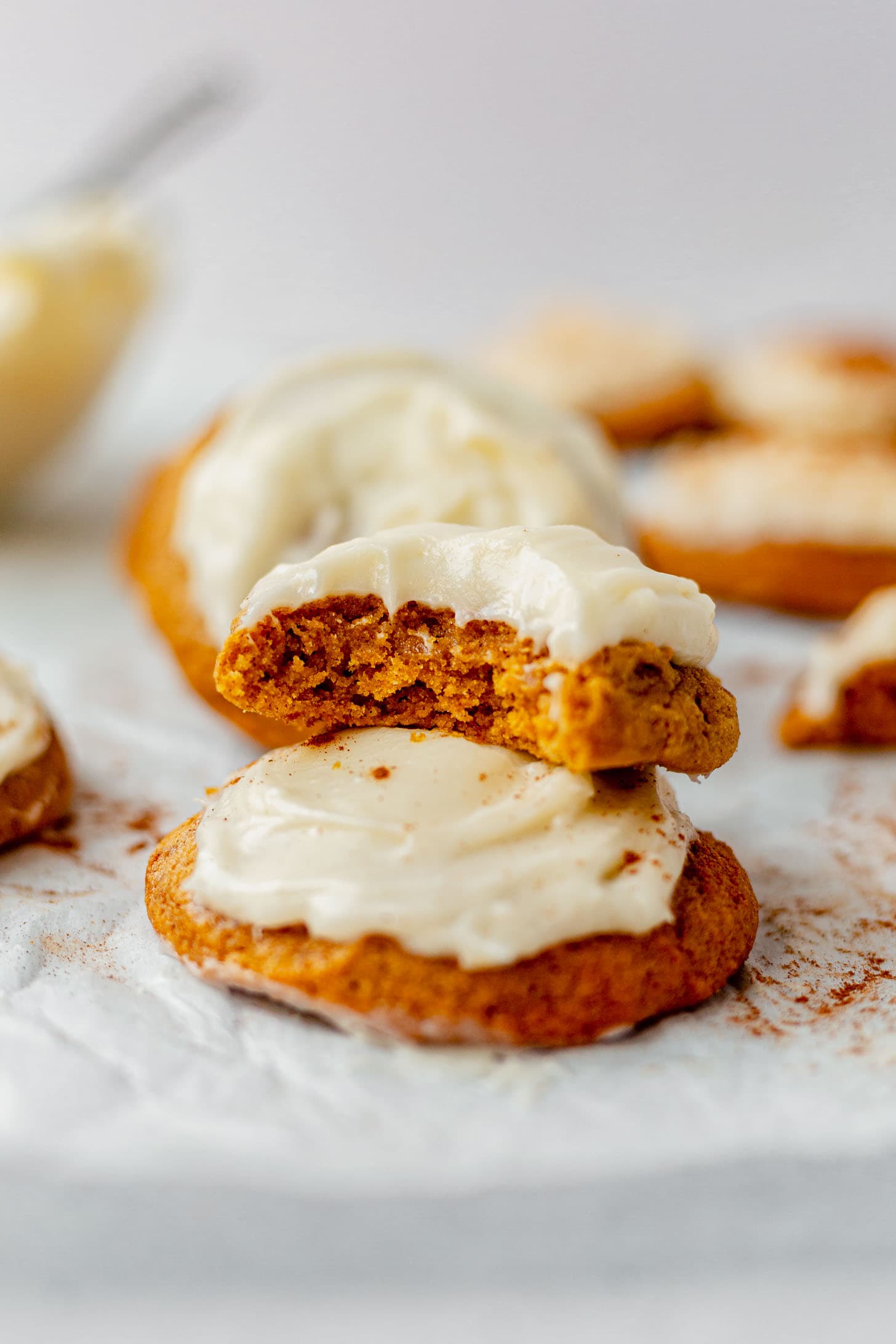 two pumpkin cookies with cream cheese frosting stacked on a piece of parchment paper.