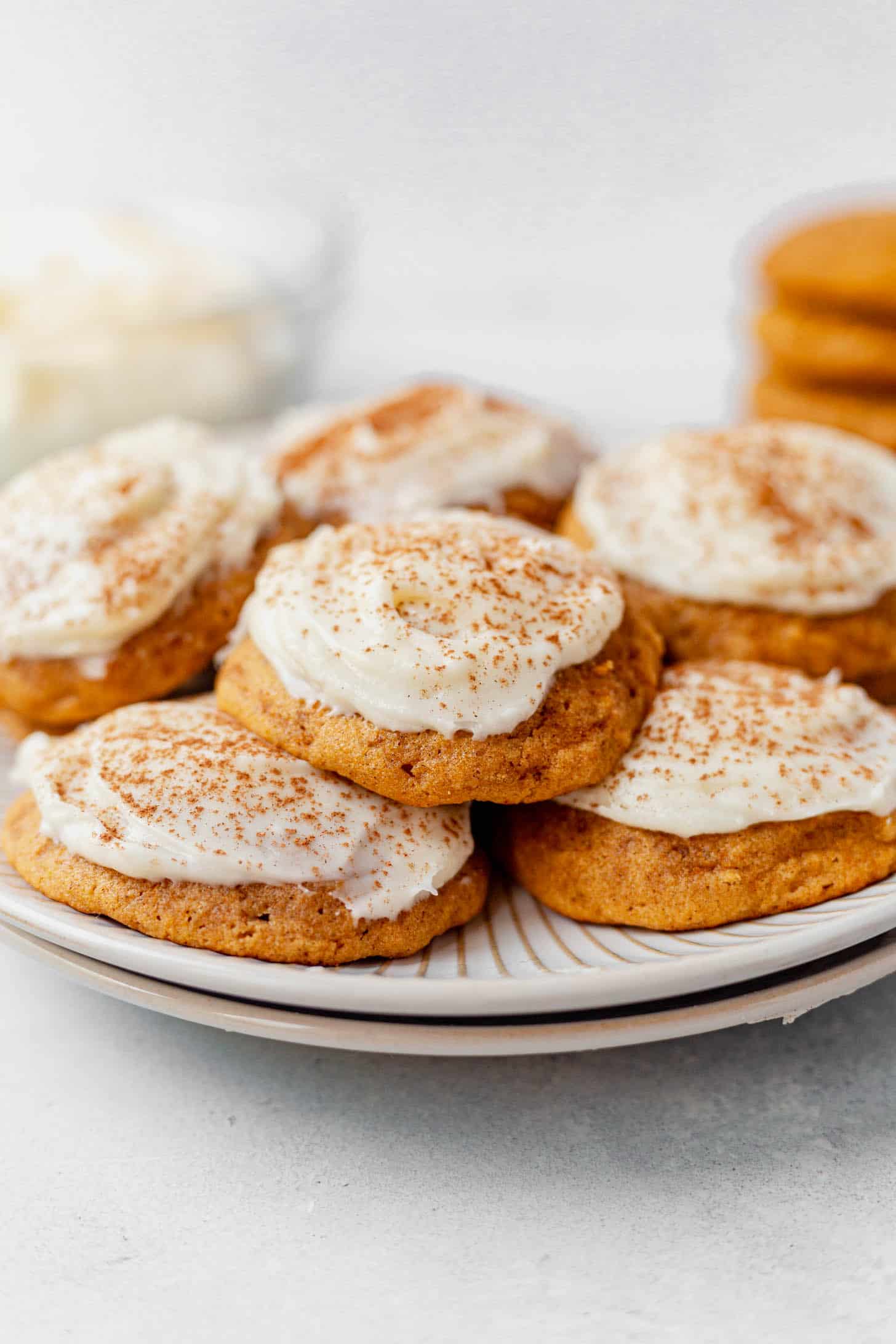 A batch of soft pumpkin cookies with cream cheese frosting on a white plate.