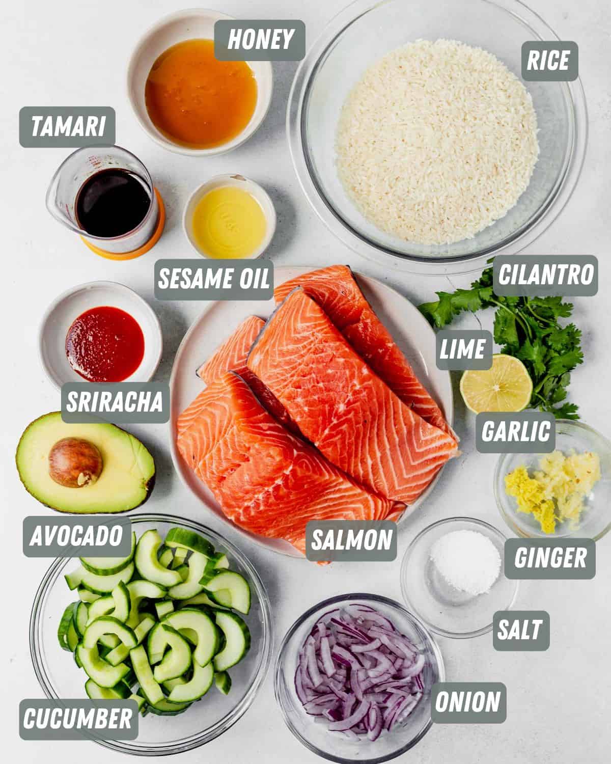 salmon filets, sauce ingredients, uncooked rice, cucumber and avocado on a table