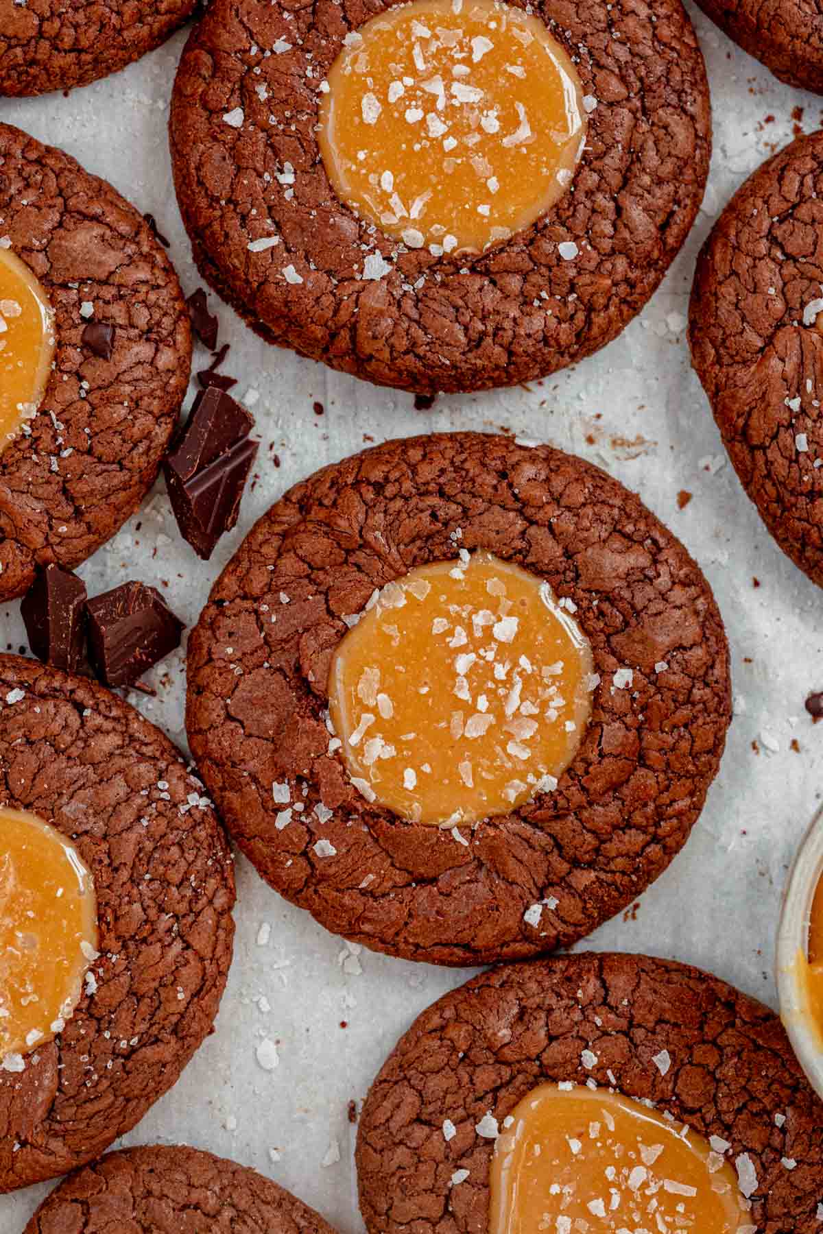salted caramel brownie cookies topped with flaky sea salt laying on parchment paper.