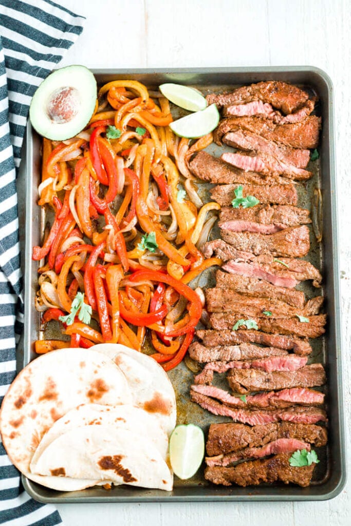 sheet pan steak fajitas on a tray with avocado, cilantro and toasted toritillas