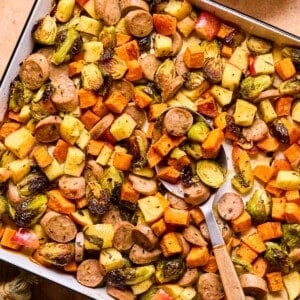 sheet pan full of maple dijon sausage and veggies with a spoon scooping.