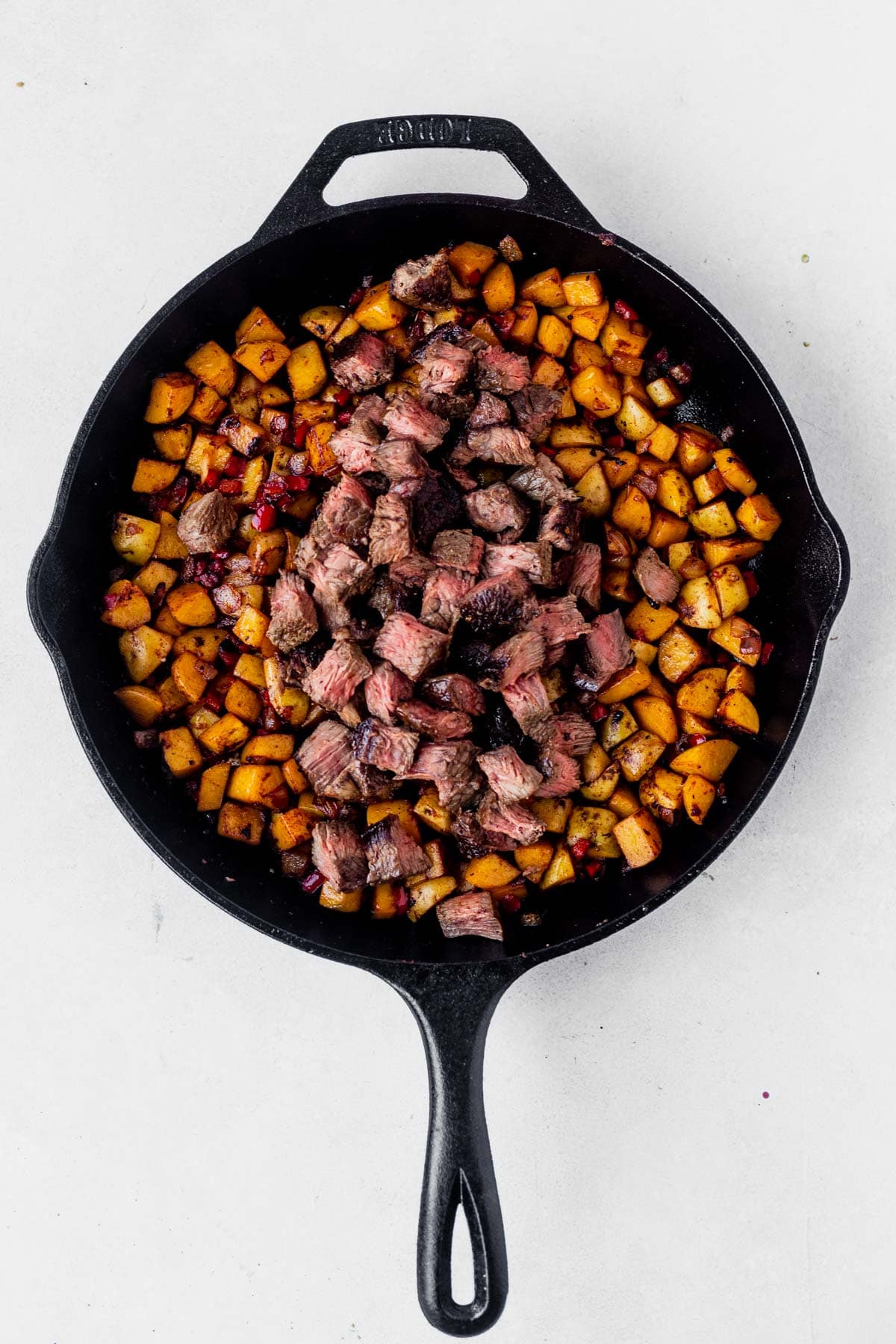 cubed steak overtop of hashbrown potatoes in a skillet
