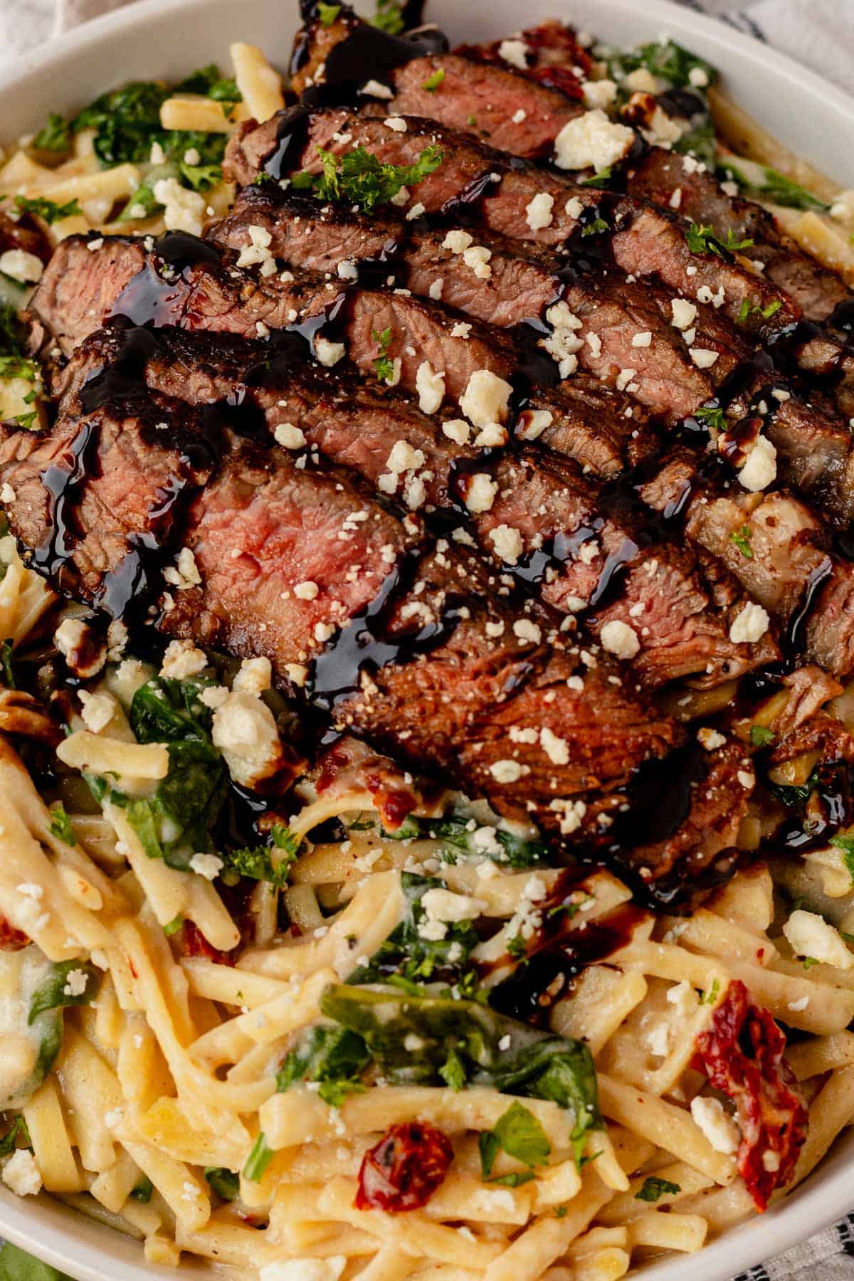 steak pasta in a white bowl with balsamic glaze.