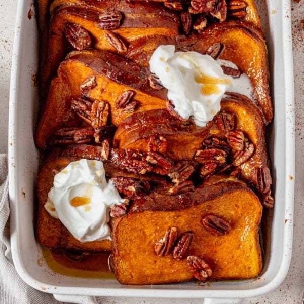 stuffed pumpkin french toast in a casserole dish with syrup and whipped cream.