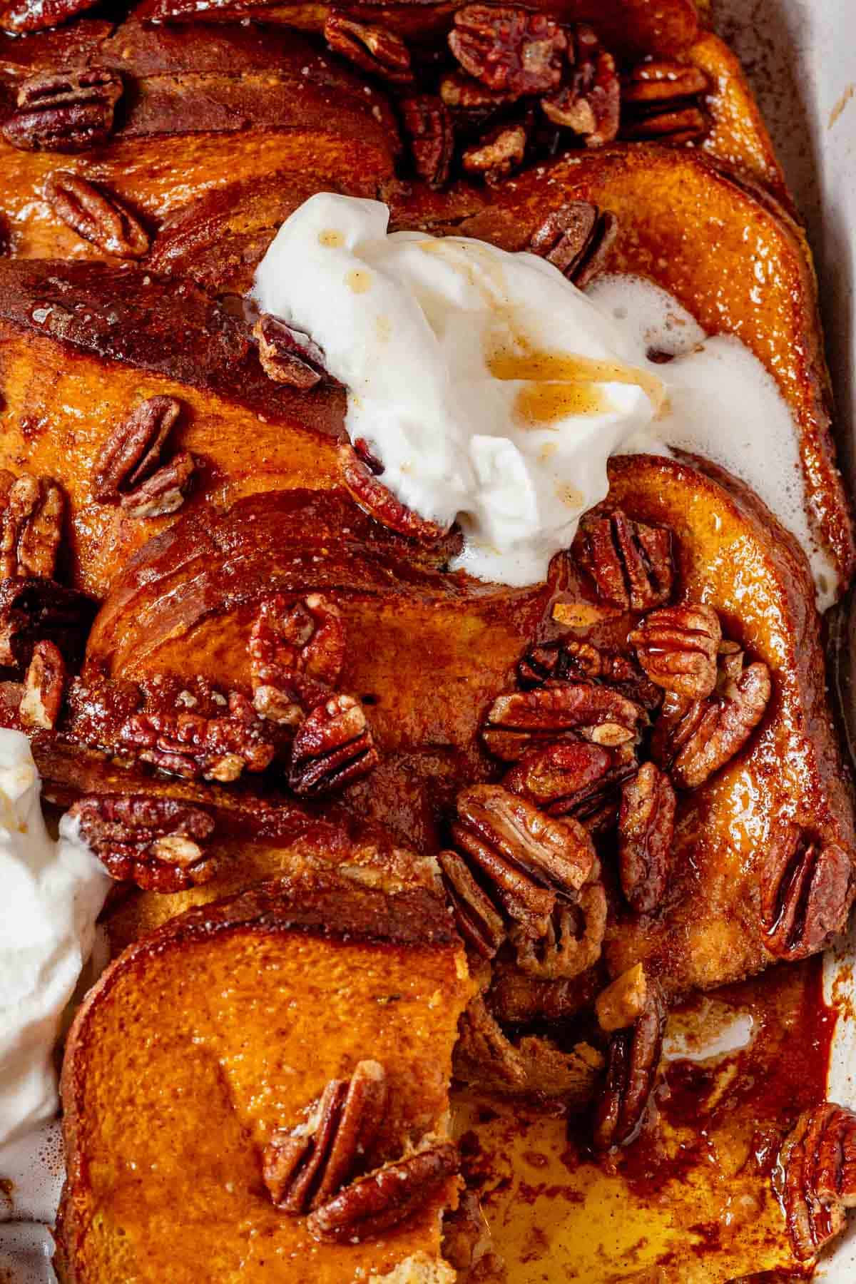 a piece of stuffed pumpkin french toast topped with pecans and whipped cream.