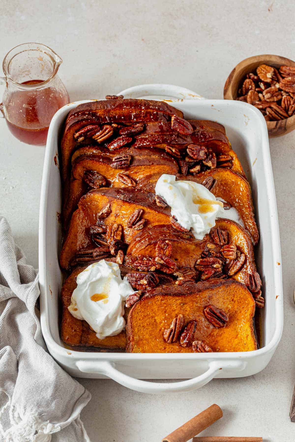 stuffed pumpkin french toast in a casserole dish with whipped cream and pecans.
