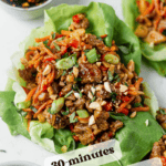 pork lettuce wrap sitting on a counter wtih a bowl of teriyaki dressing and chopped green onions